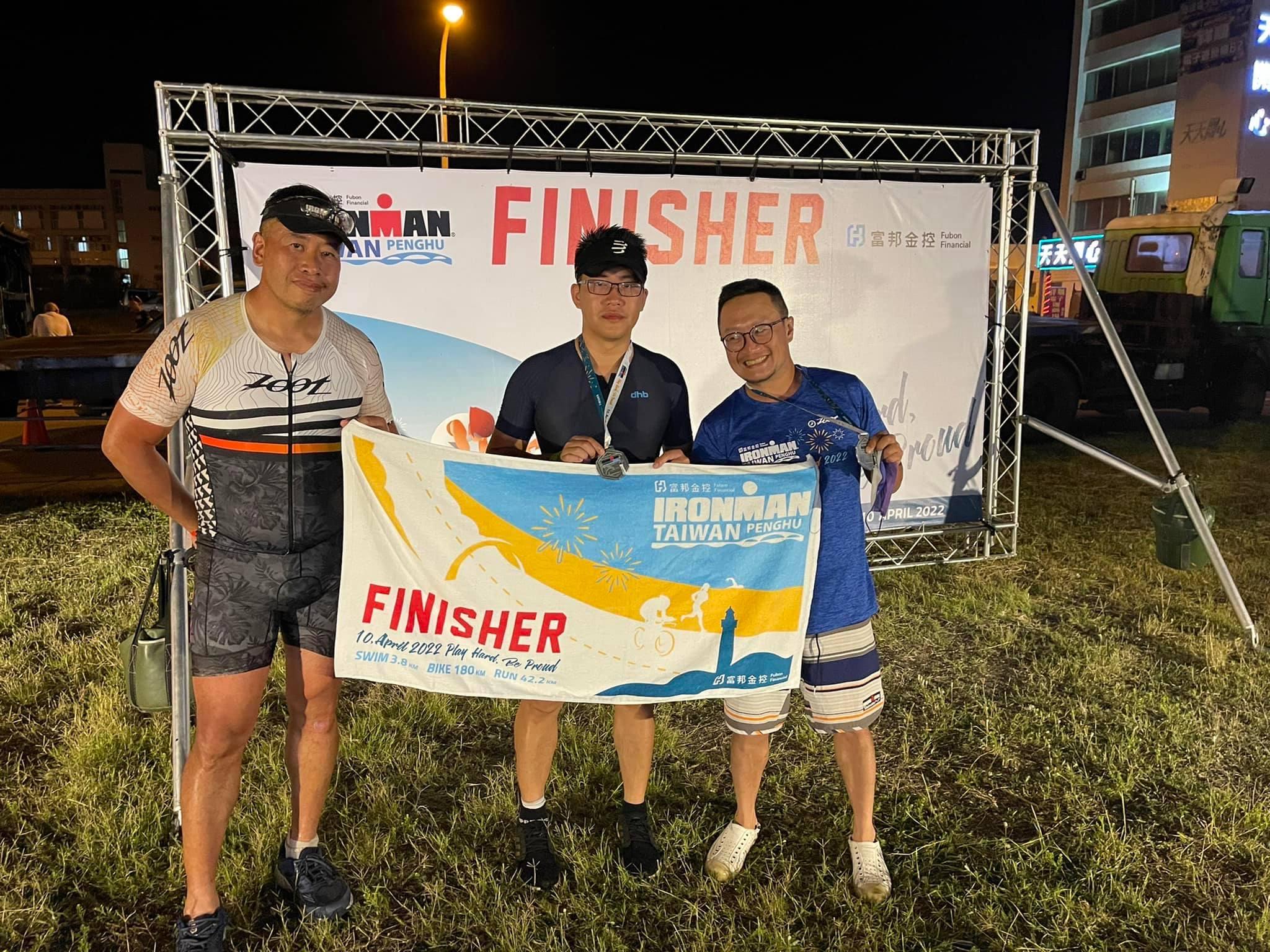 三位選手手持完賽毛巾與獎牌在終點線合影