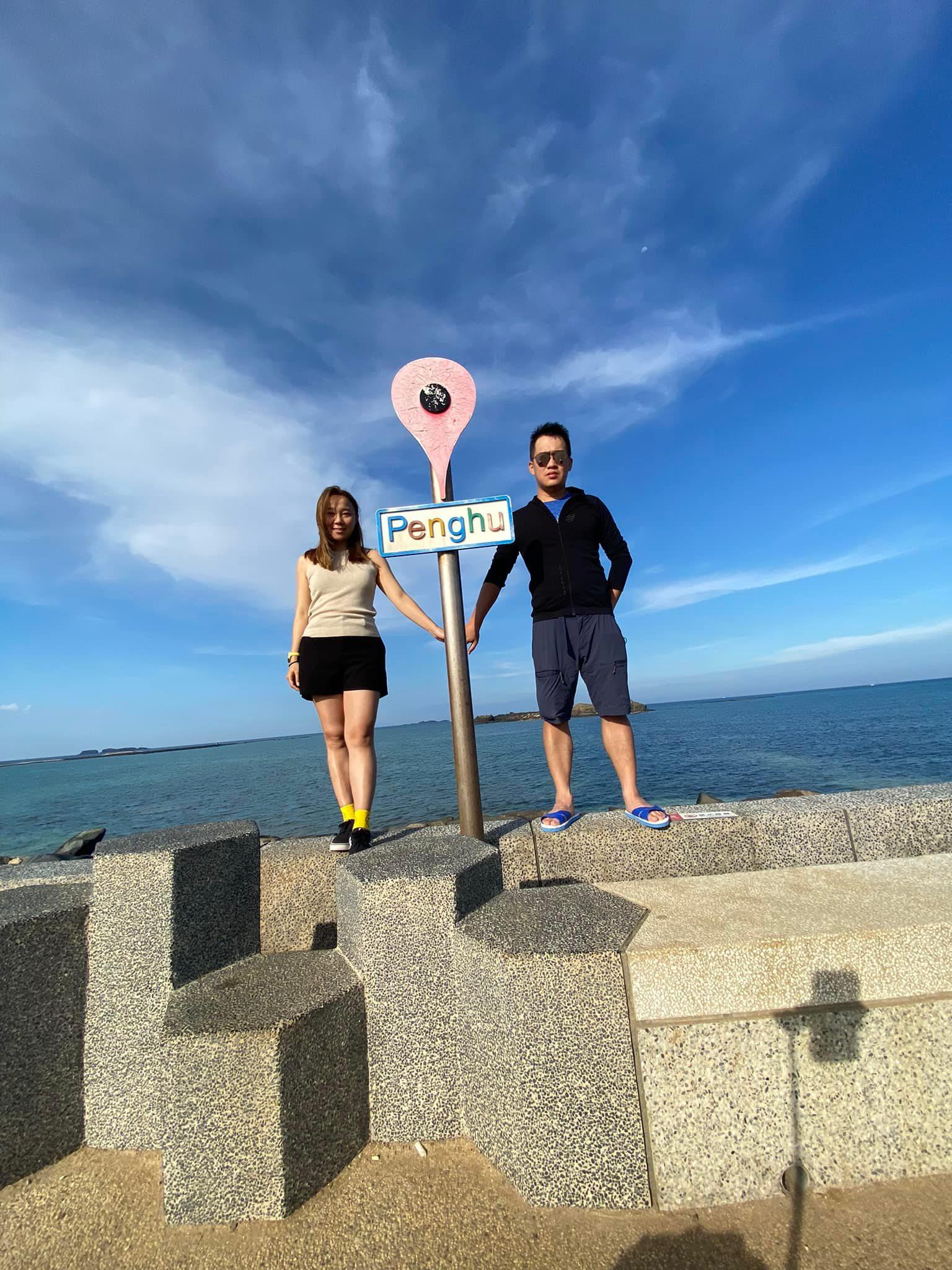 Two people holding Penghu map pin sign by the ocean