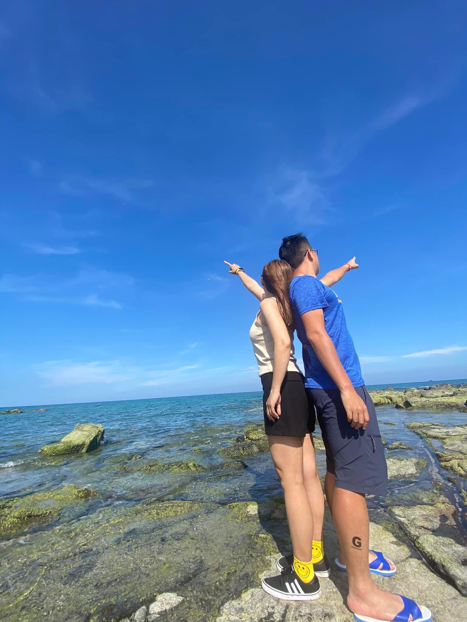 Two people back-to-back pointing at the horizon over rocky shore